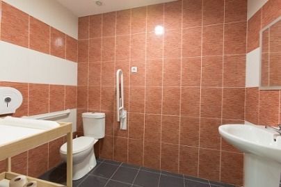 Baño accesible con paredes de azulejos rojos, detalles blancos y barra de seguridad.