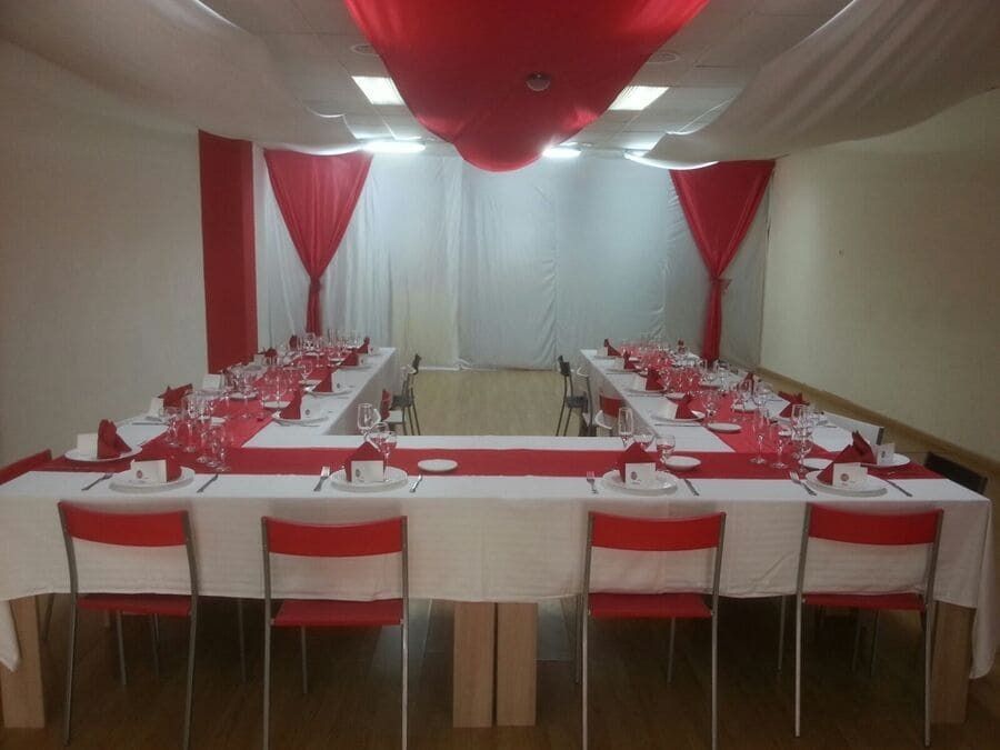 Comedor decorado en rojo y blanco con mesa en forma de U preparada para celebración; sillas y cortinas en el techo.