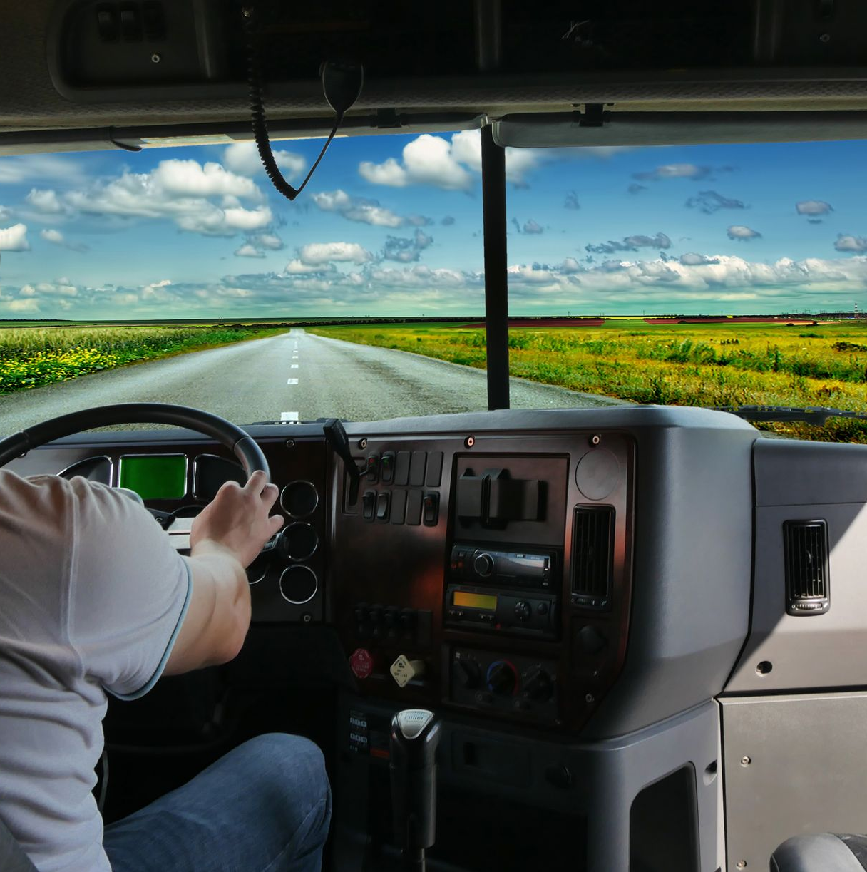Vista del conductor del camión: manos en el volante, conduciendo por una carretera abierta con cielo azul y campos.