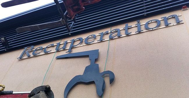 Enseigne de réception sur une façade beige, avec logo bleu et volets métalliques.