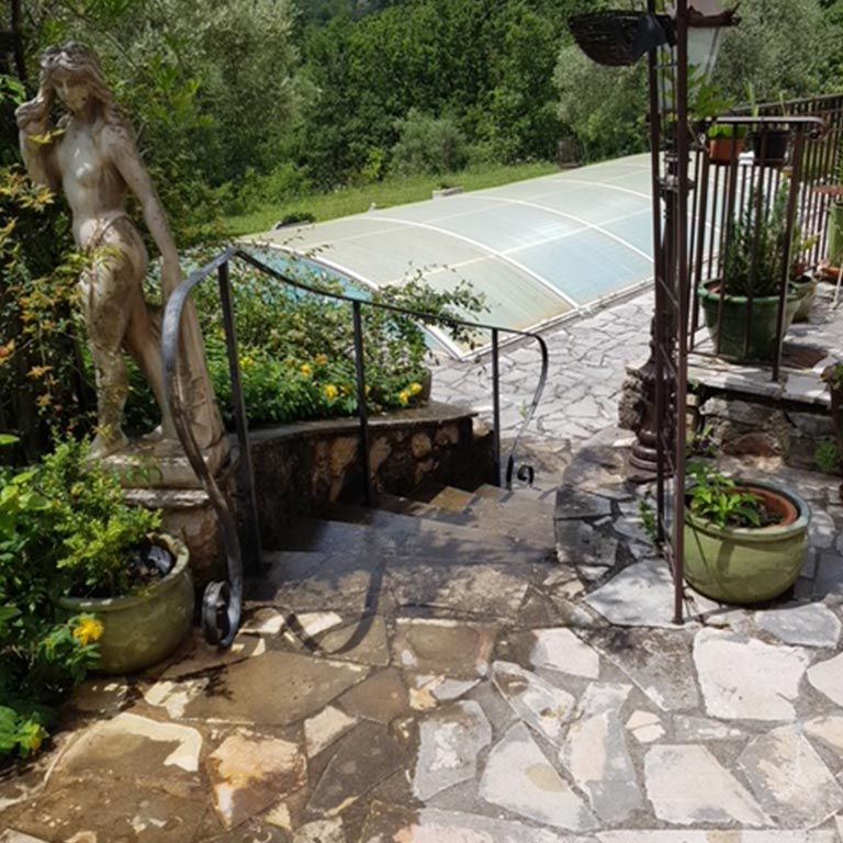 Jardin en pierre avec plantes en pot, une statue nue et une serre incurvée