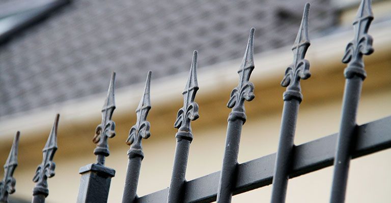 Clôture en fer forgé noir avec des embouts décoratifs pointus sur un fond beige flou