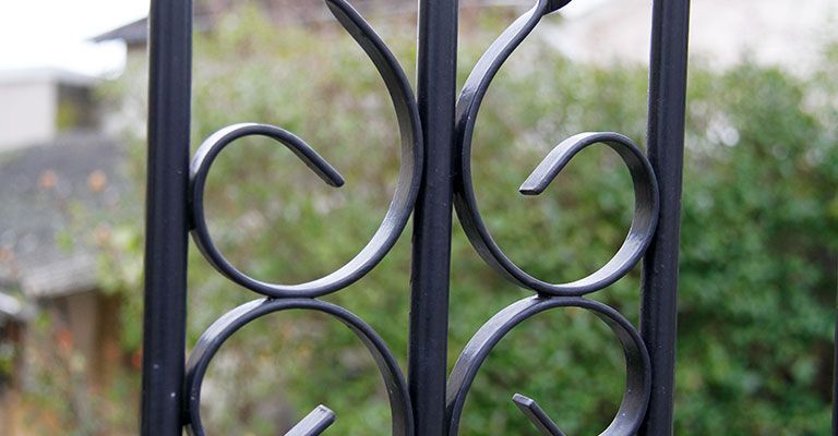Portail en fer forgé noir orné de volutes circulaires sur fond de jardin flou.