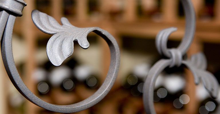 Gros plan sur une grille en métal gris ornée de volutes et de détails blancs en forme de feuille.