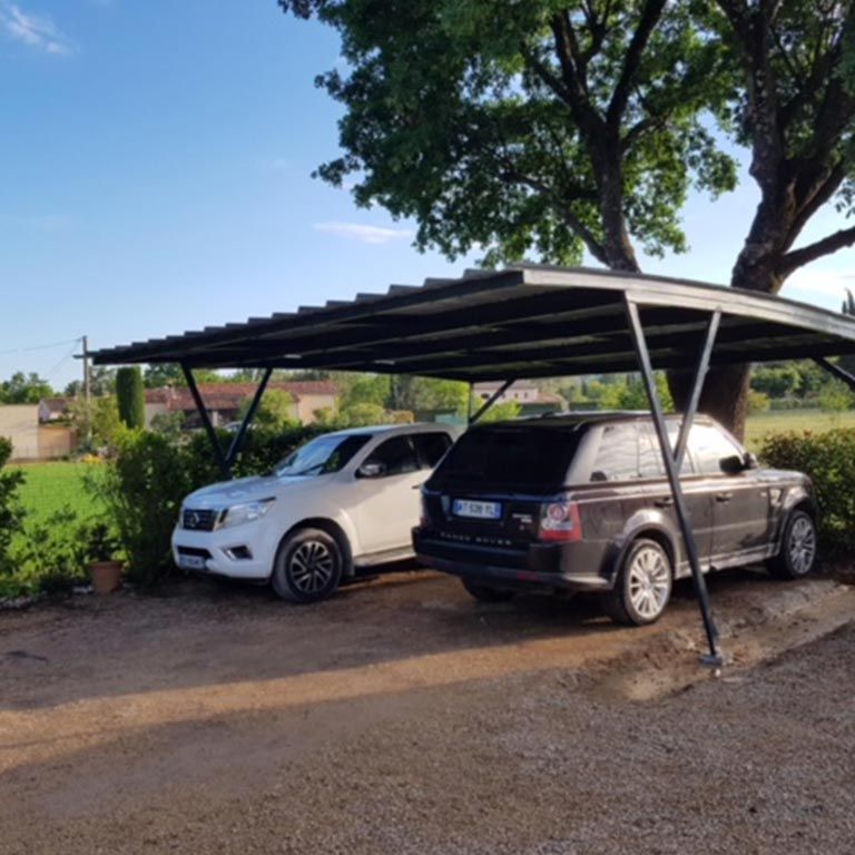 Deux SUV stationnés sous un abri métallique, à côté d'un arbre, par une journée ensoleillée.