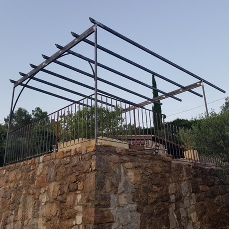 Terrasse en pierre en construction avec charpente et rambarde en métal noir sur fond de ciel nuageux