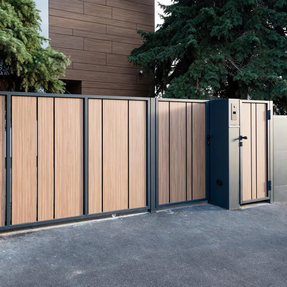 Portail moderne en bois avec un petit portail, jouxtant un bâtiment en briques et des arbres.