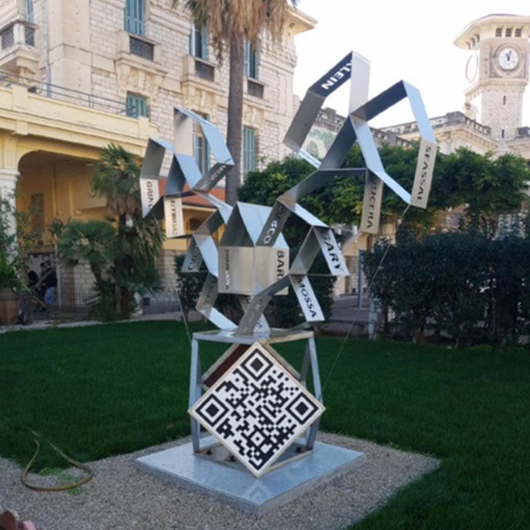 Sculpture abstraite moderne en métal avec code QR dans une cour paysagée, avec une tour d'horloge en arrière-plan
