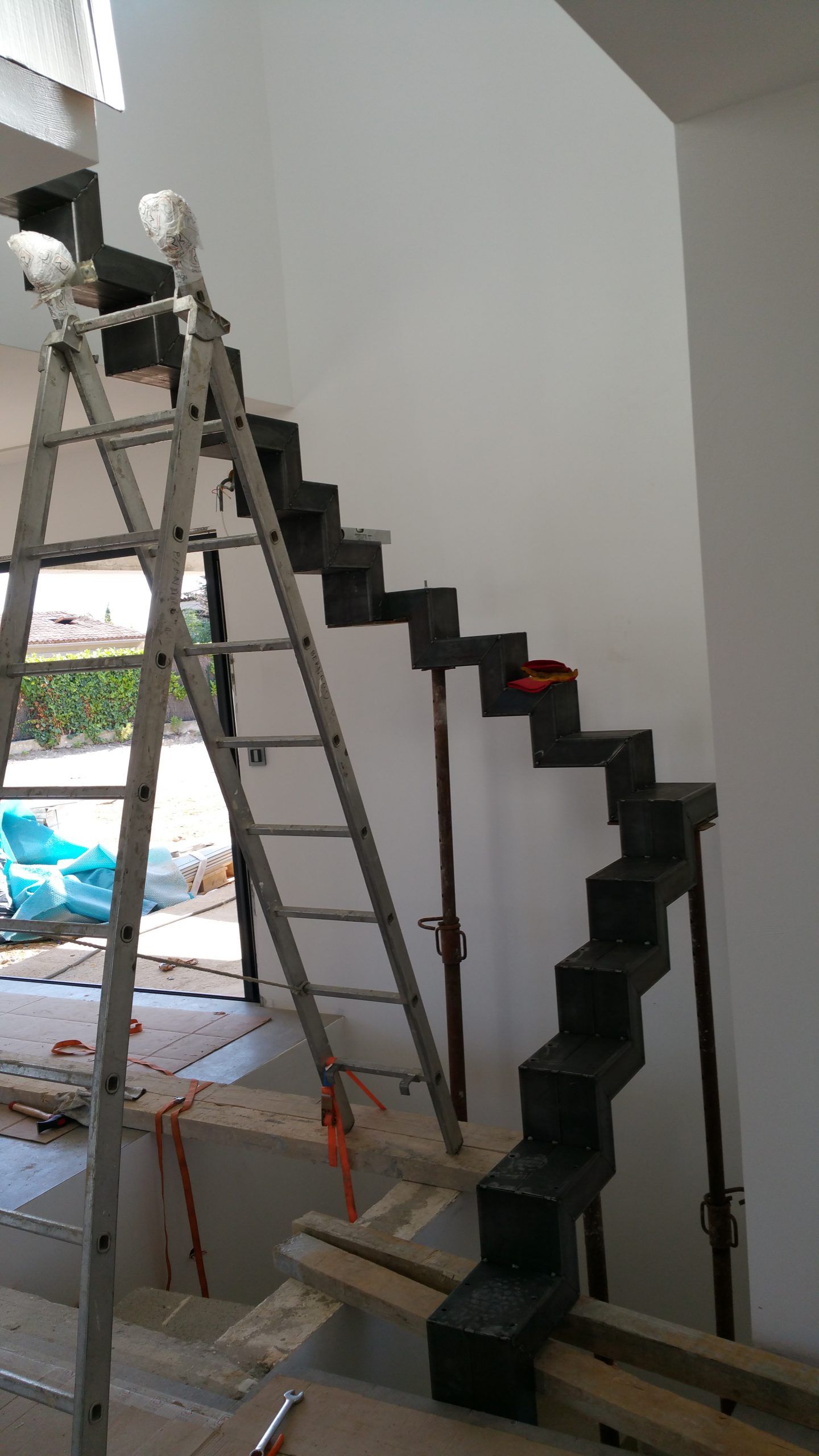 Un ouvrier sur une échelle installe un escalier noir en zigzag à l'intérieur.