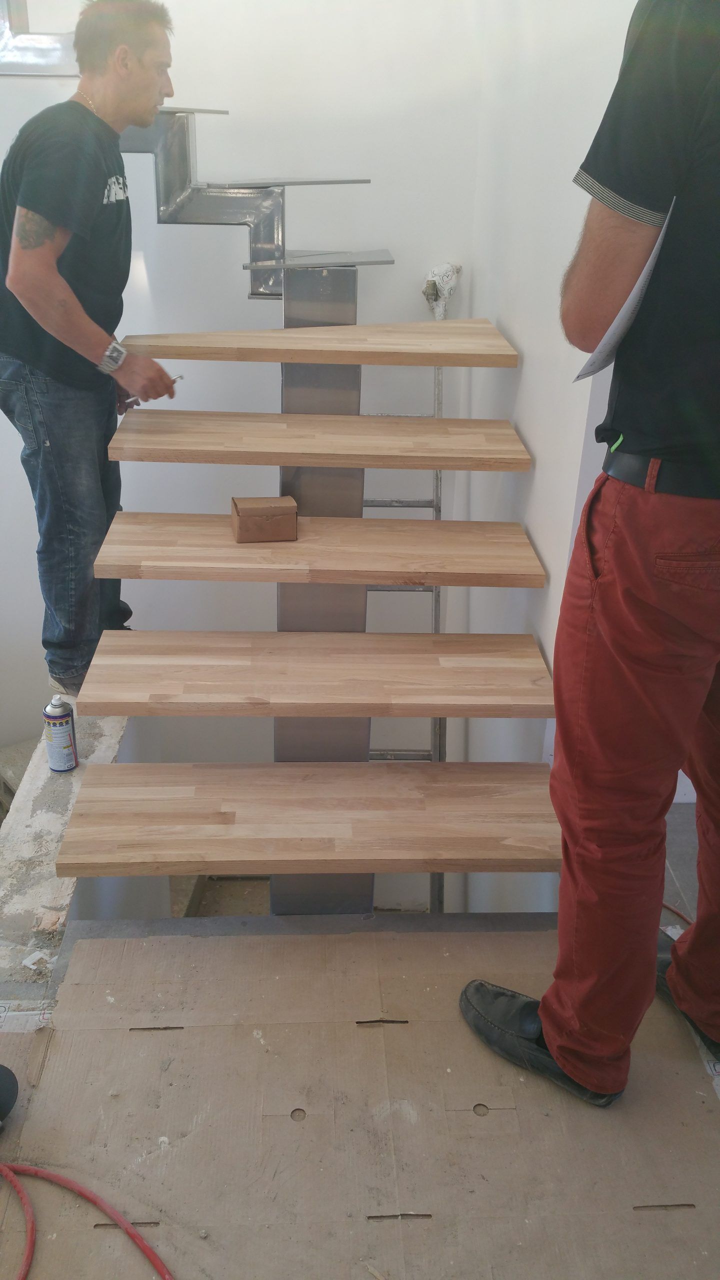 Deux personnes transportent un escalier en bois empilé dans un couloir étroit.
