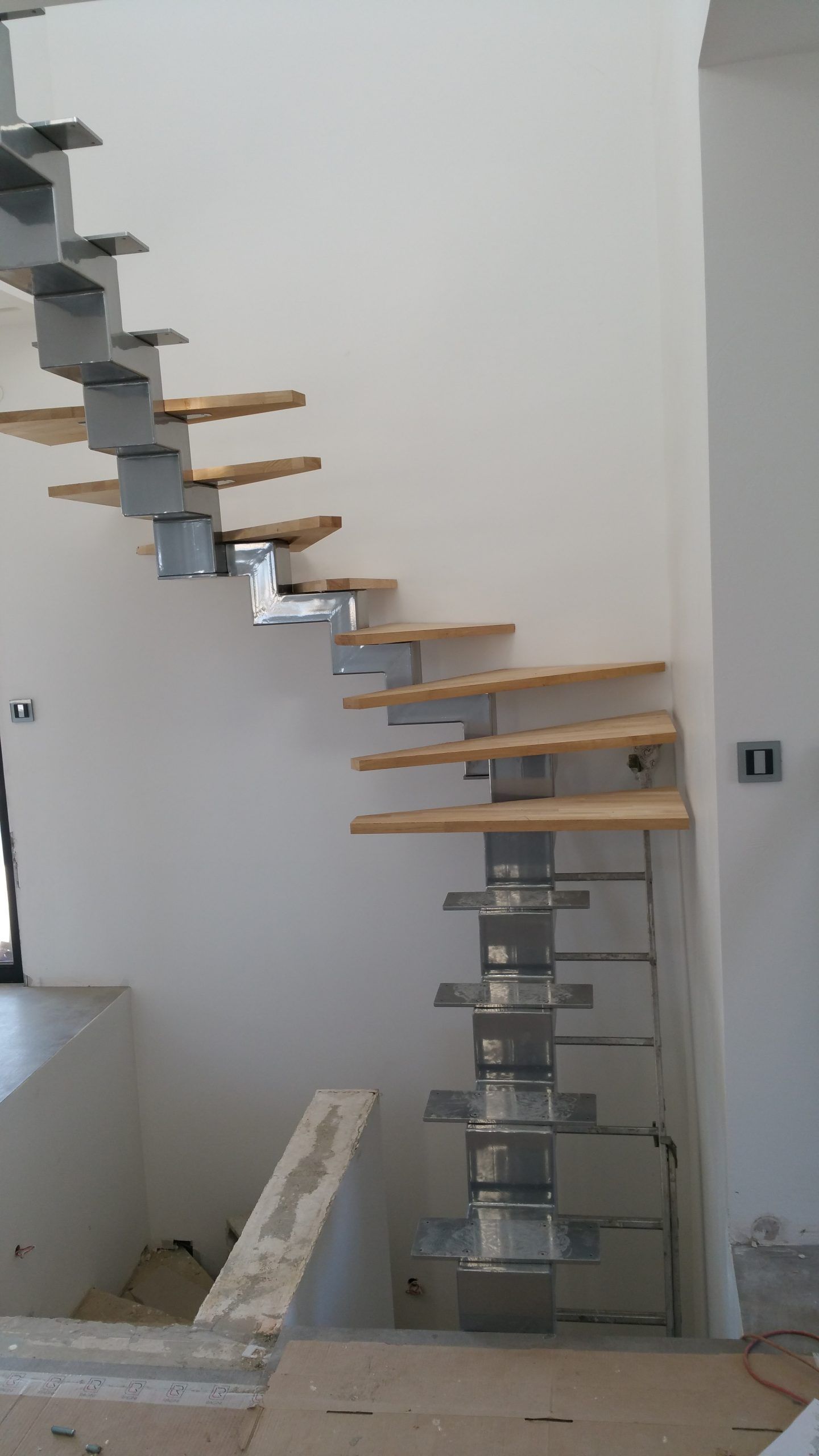 Escalier flottant partiellement construit avec supports métalliques et marches en bois dans une pièce intérieure blanche