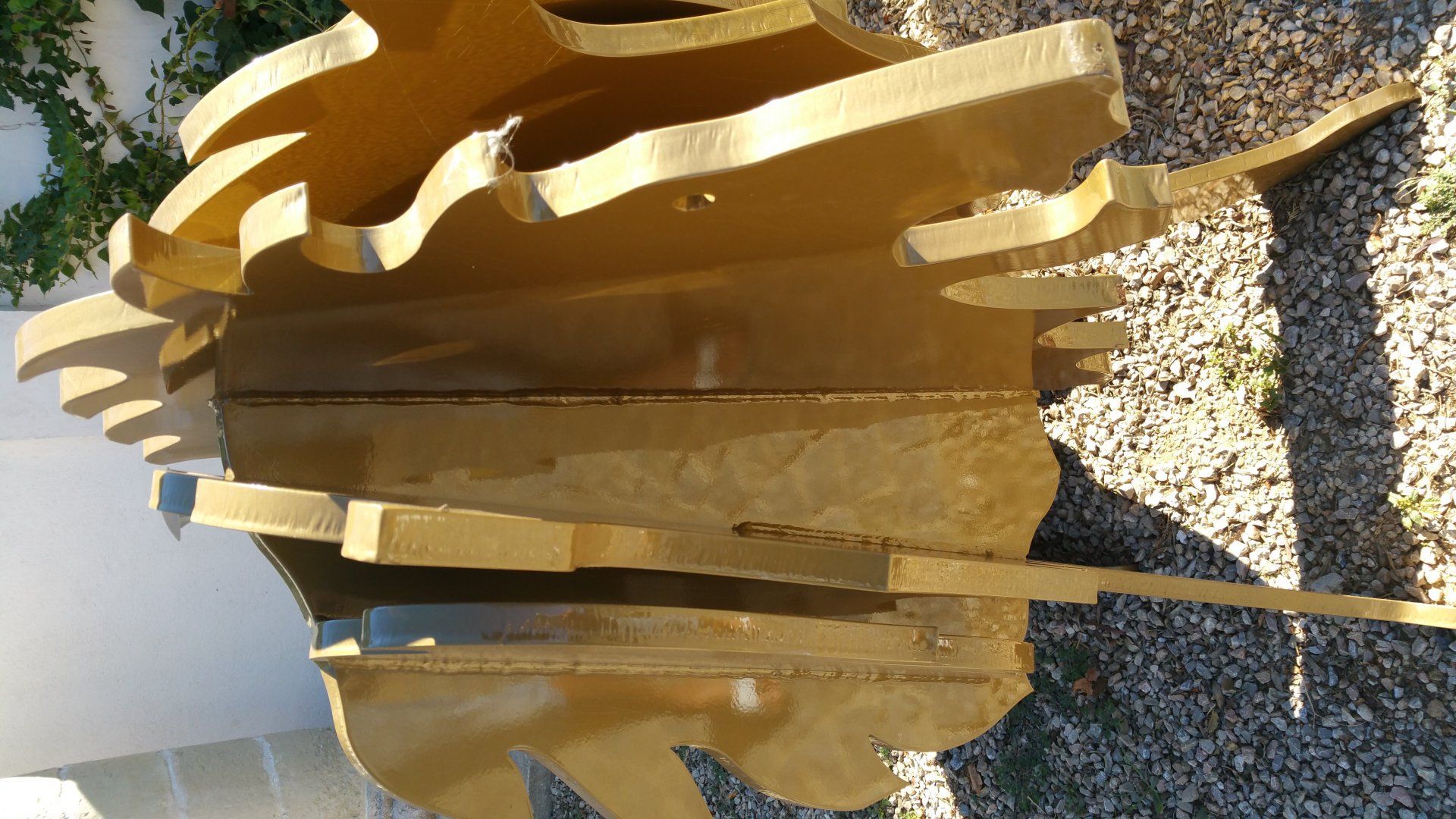 Sculpture abstraite en métal doré, composée de bandes courbes superposées projetant des ombres au soleil.