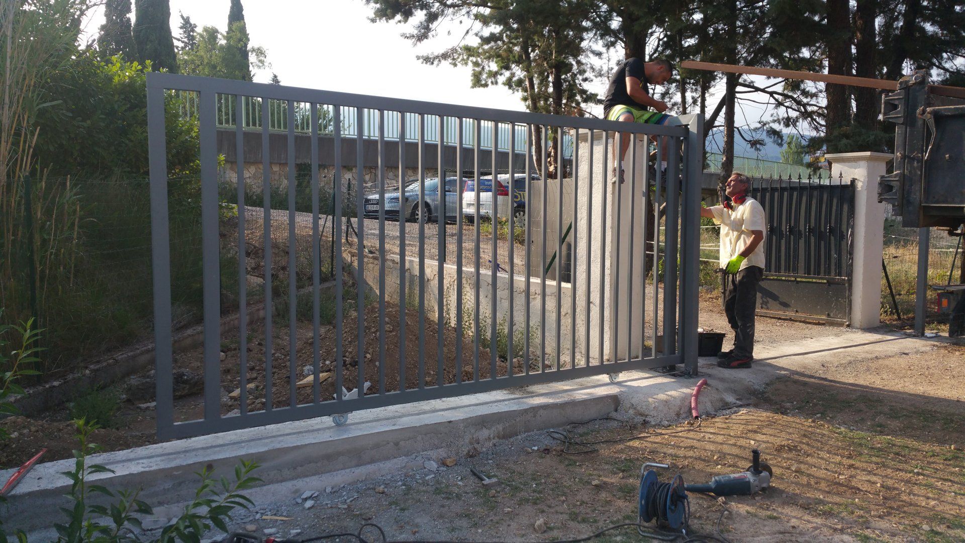 Un ouvrier installe un grand portail coulissant en métal à l'entrée d'une allée de gravier.
