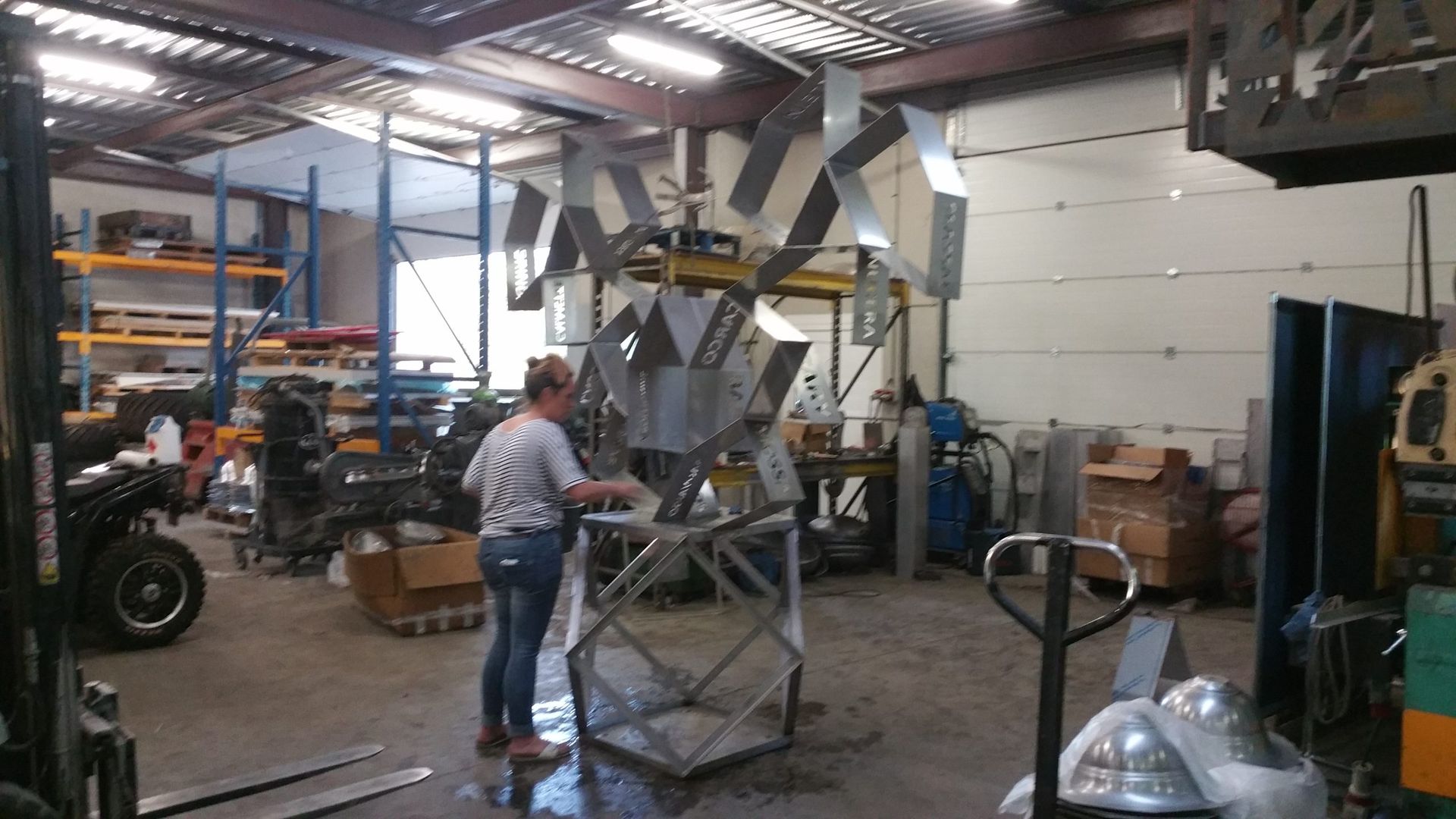 Une personne se tient à côté d'une grande machine industrielle en métal dans un atelier avec des étagères et des outils.