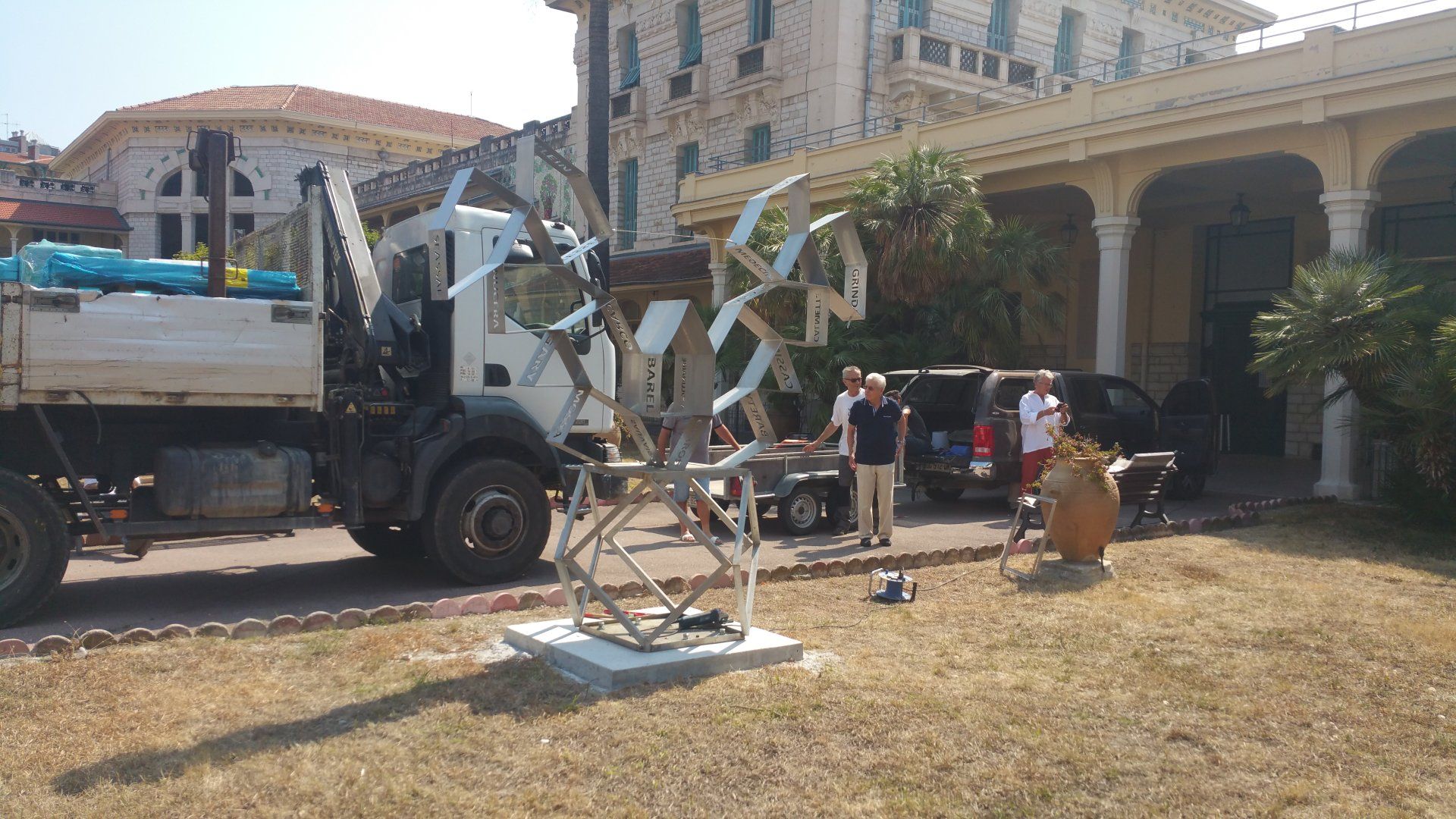 Camion utilitaire blanc et ouvriers manœuvrant une nacelle élévatrice à l'extérieur d'un bâtiment en stuc en plein jour