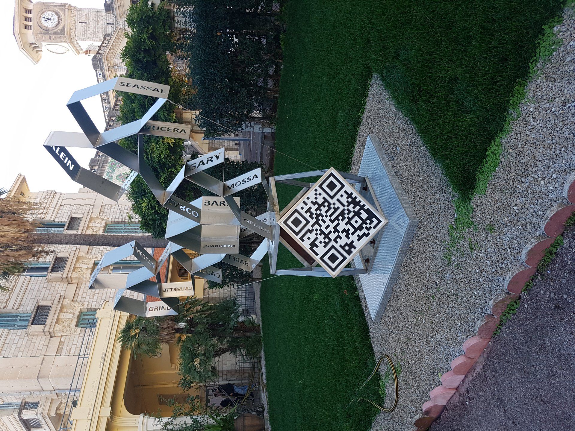 Sculpture extérieure de rubans métalliques sur une pelouse à côté d'un panneau à code QR et d'un chemin
