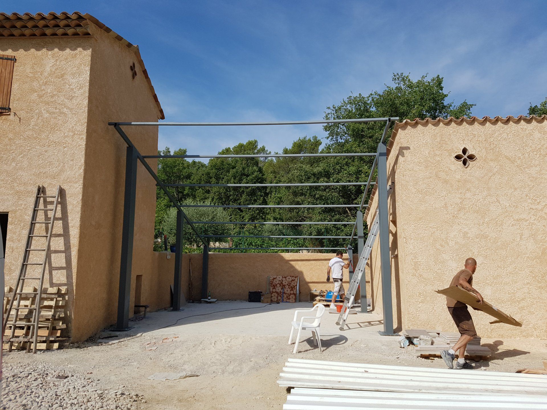 Deux personnes travaillent dans un chantier ensoleillé, à côté de murs en stuc et de poutres d'acier.