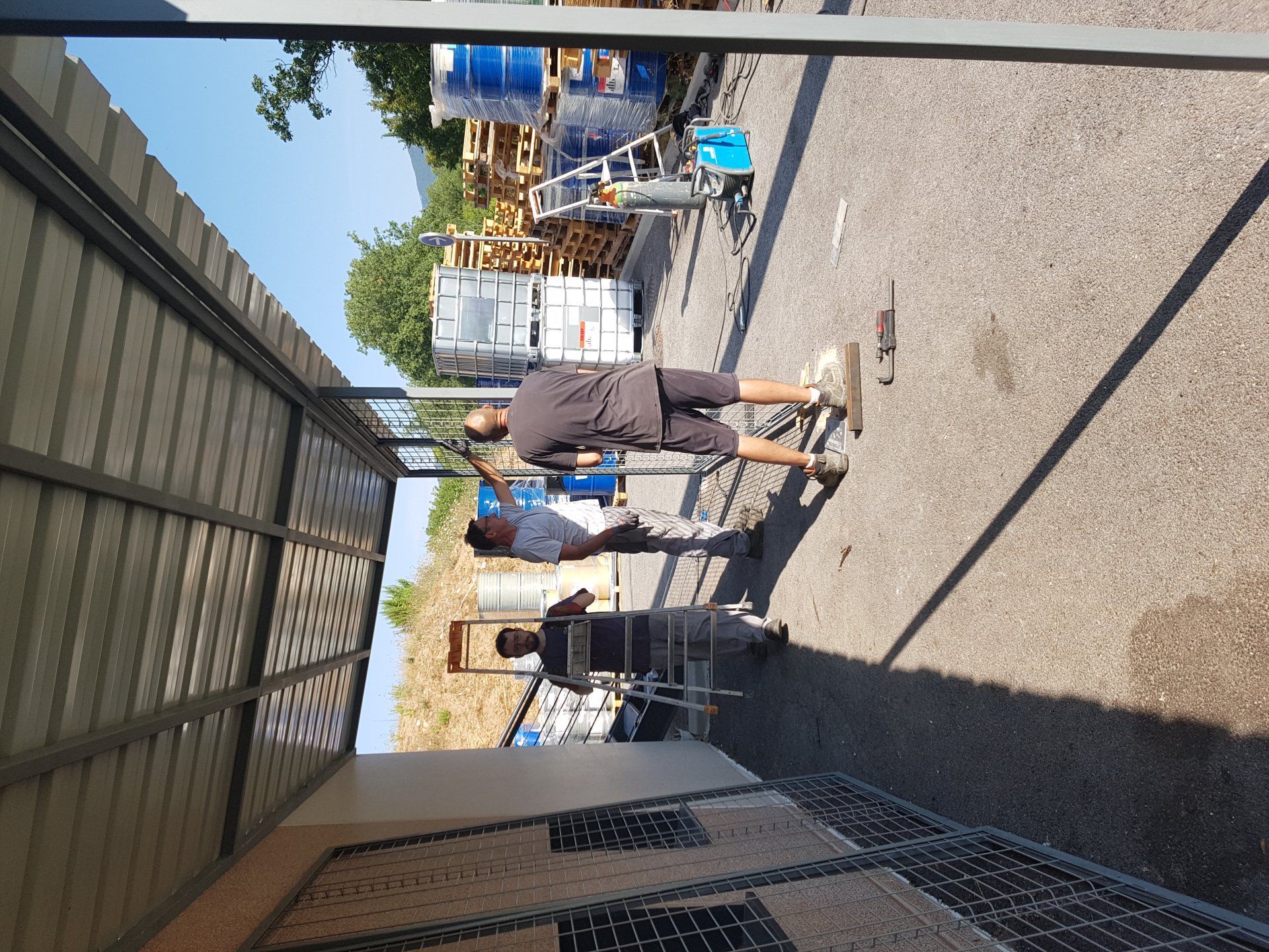 Des gens se promènent dans une allée ensoleillée d'un marché en plein air, bordée d'étals et de tentes des deux côtés.