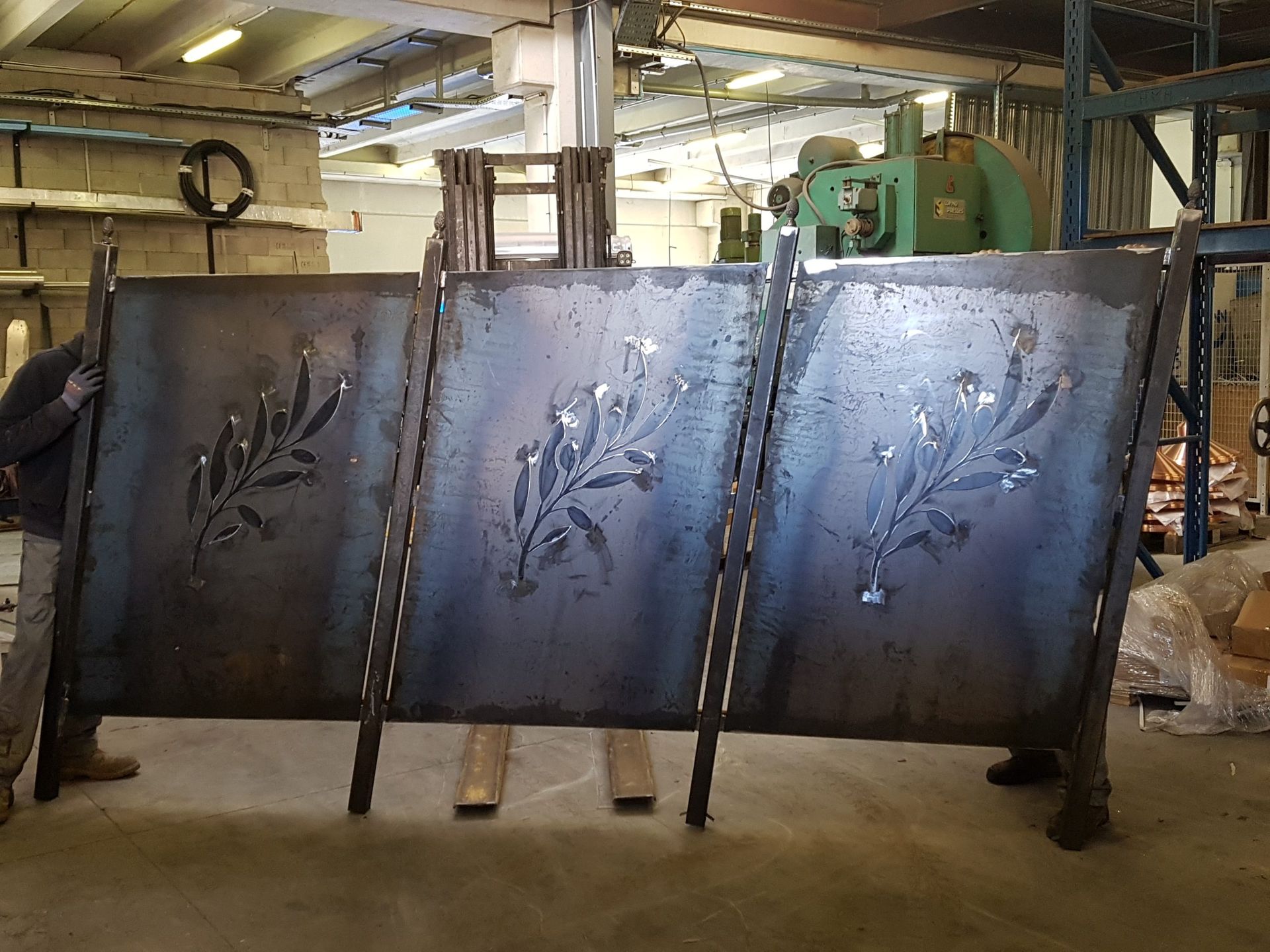 Grande lame industrielle en métal dans un atelier, avec une machine verte derrière.