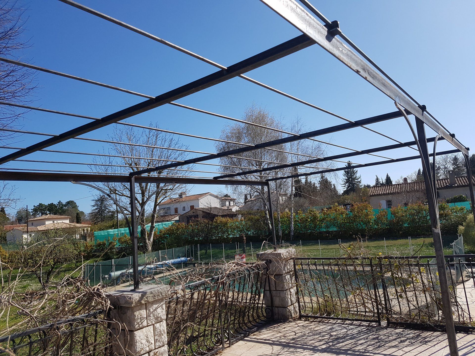 Treillis de jardin extérieur sous un ciel bleu, avec plates-bandes surélevées, arbres et filet dans une cour clôturée