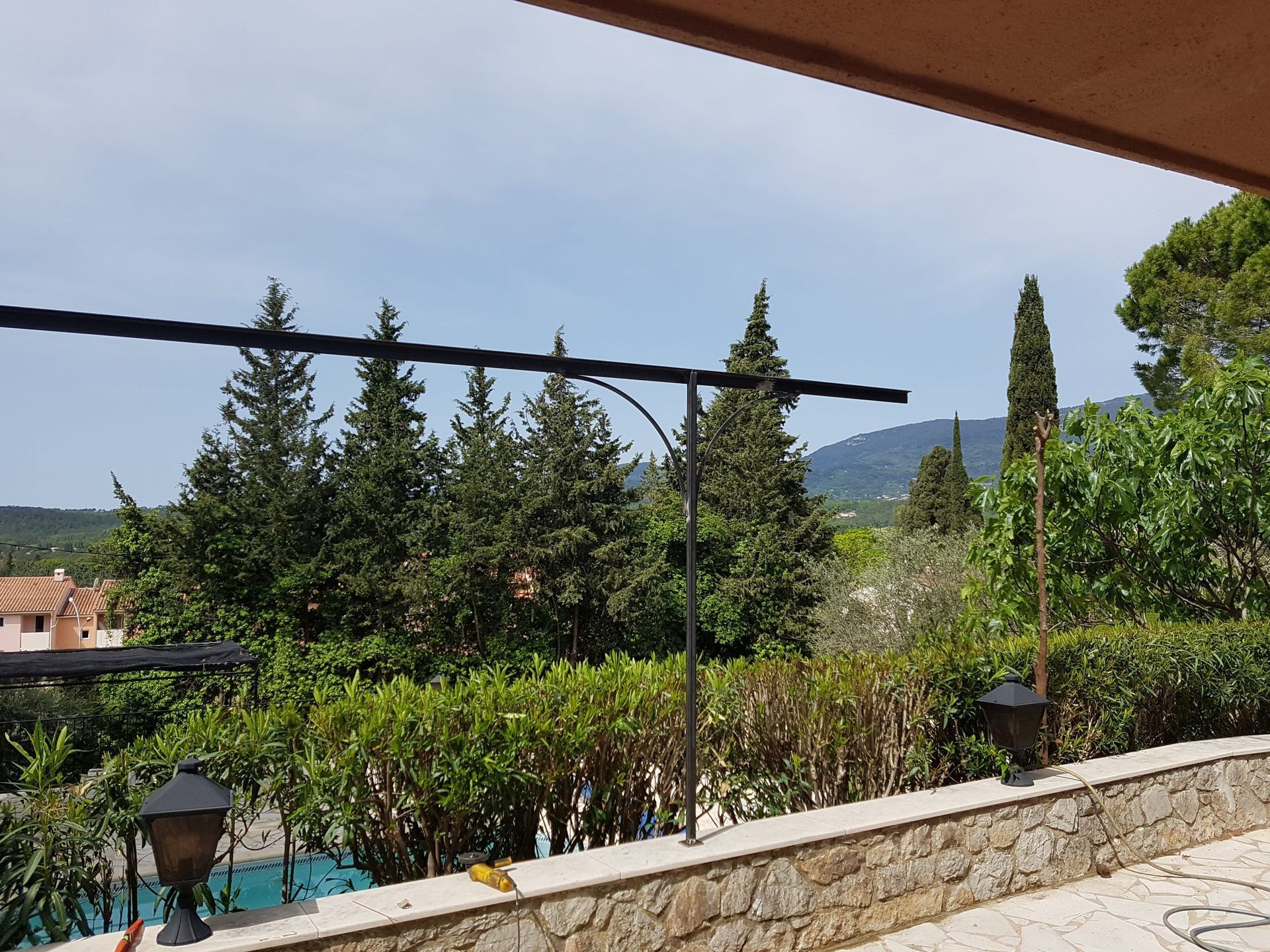 Terrasse donnant sur un jardin luxuriant et des collines au loin, avec une lanterne et un avant-toit en vue.