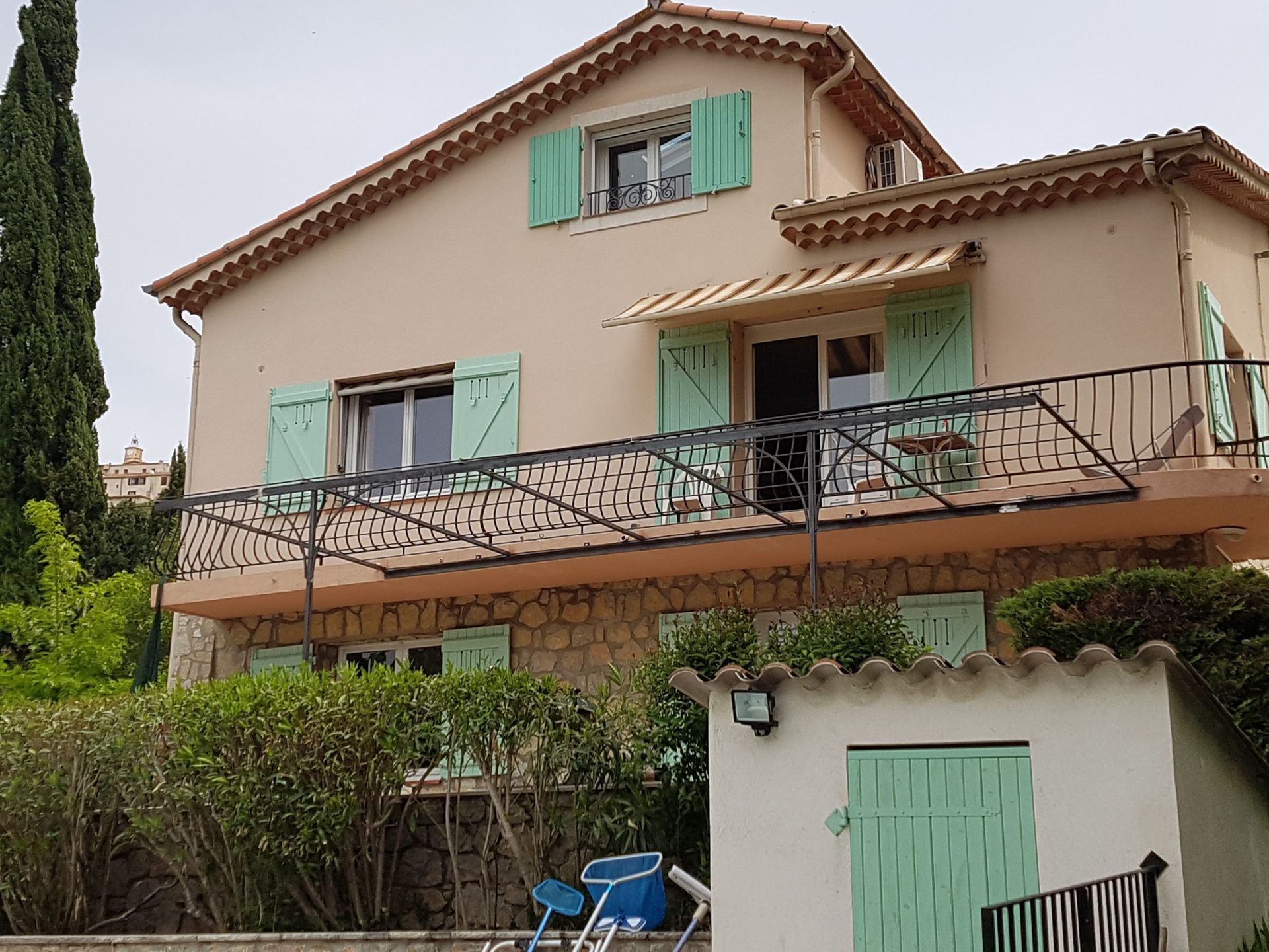 Maison de style méditerranéen avec volets verts, balcon et petit portail de jardin sous un ciel nuageux