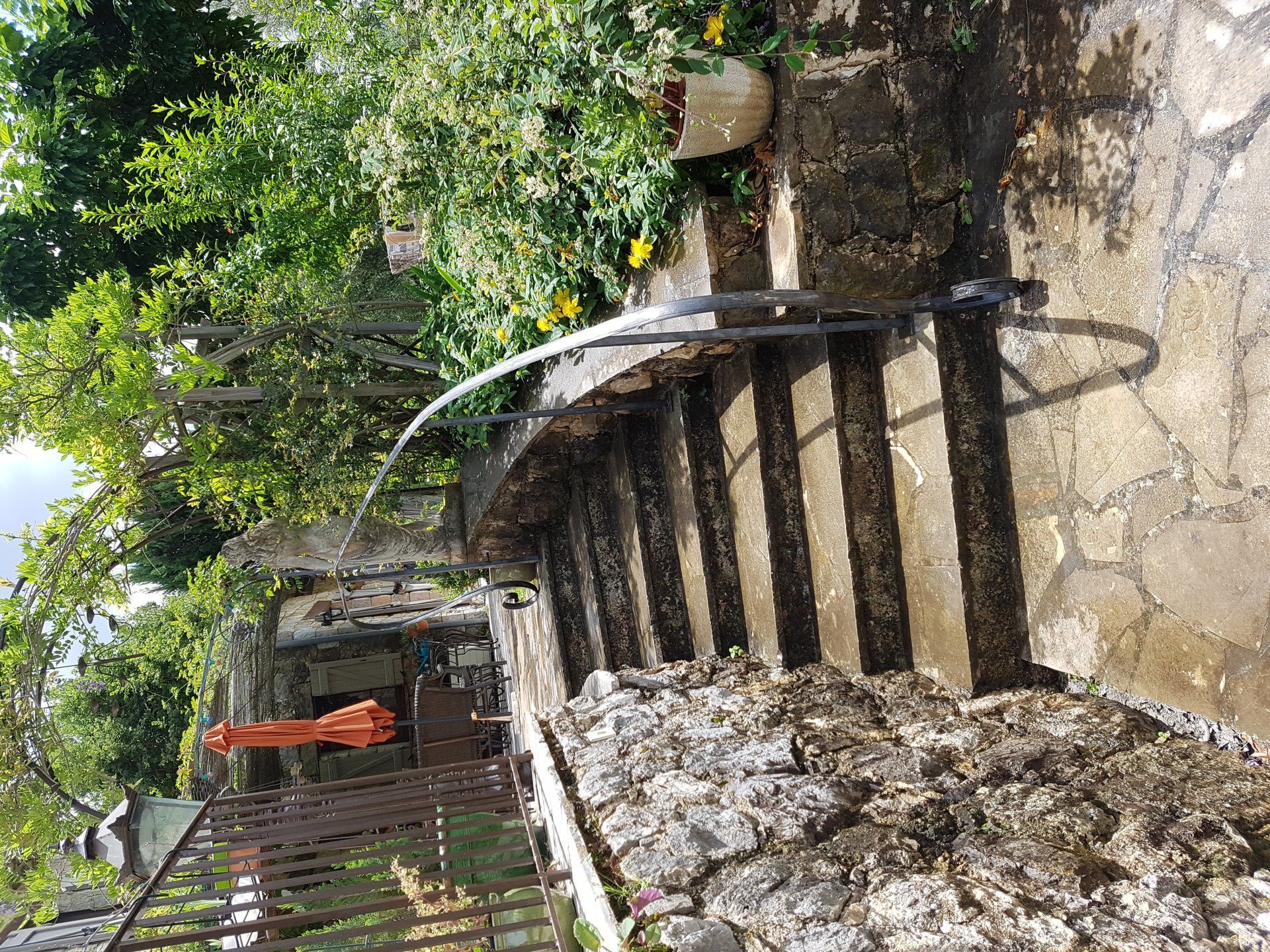 Escalier extérieur abrupt longeant un mur de pierre, avec des arbres et une lumière du soleil éclatante au-dessus.