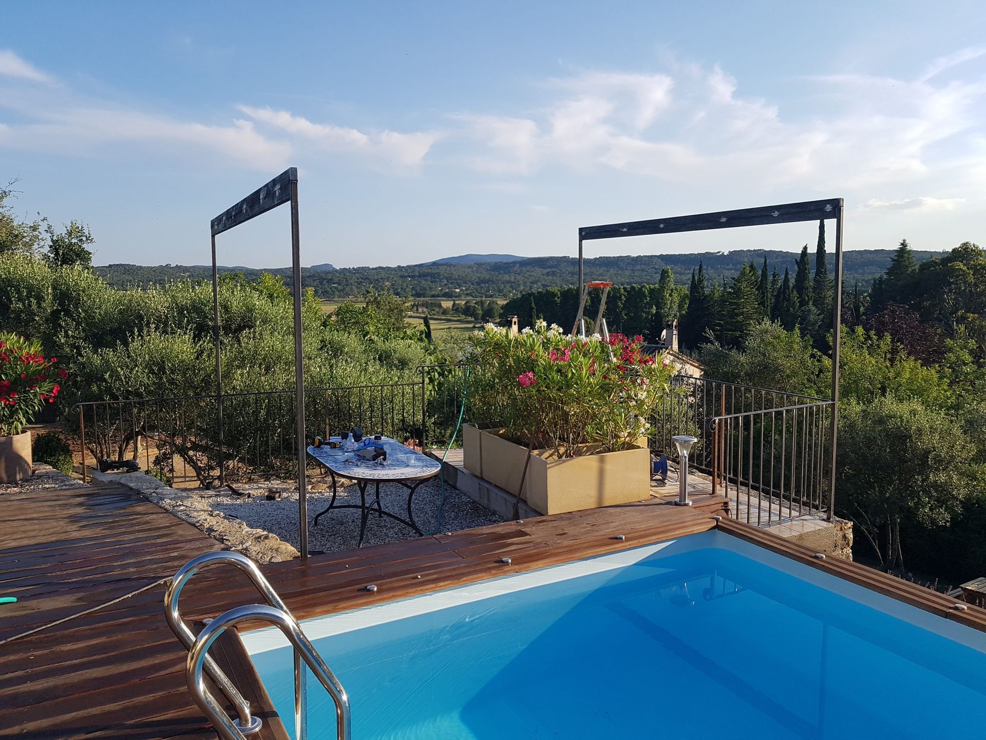 Terrasse arrière avec piscine, pergola et fleurs en pot donnant sur un paysage pittoresque