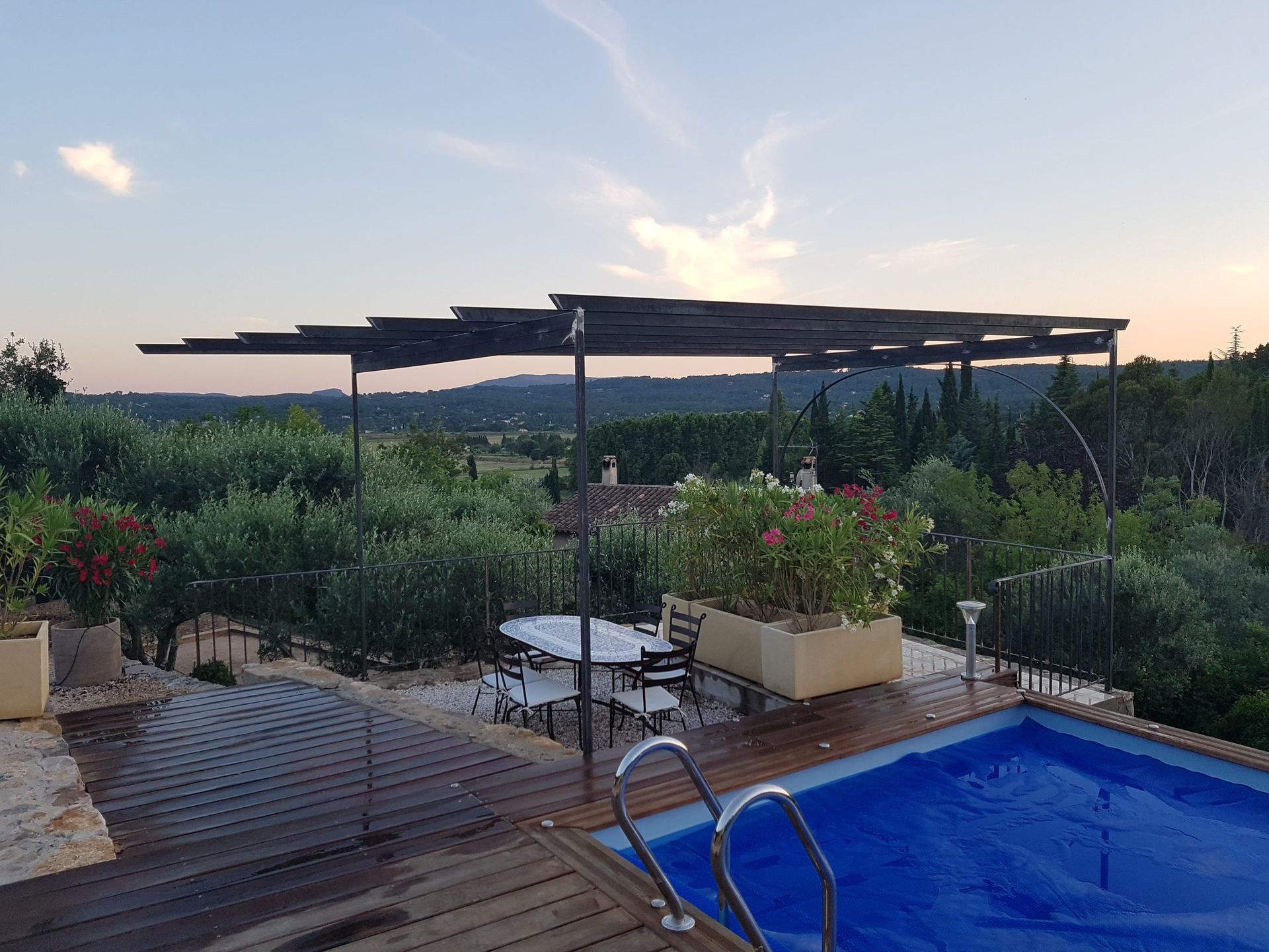 Terrasse au bord de la piscine avec piscine bleue, chaise longue, pergola et jardin au coucher du soleil