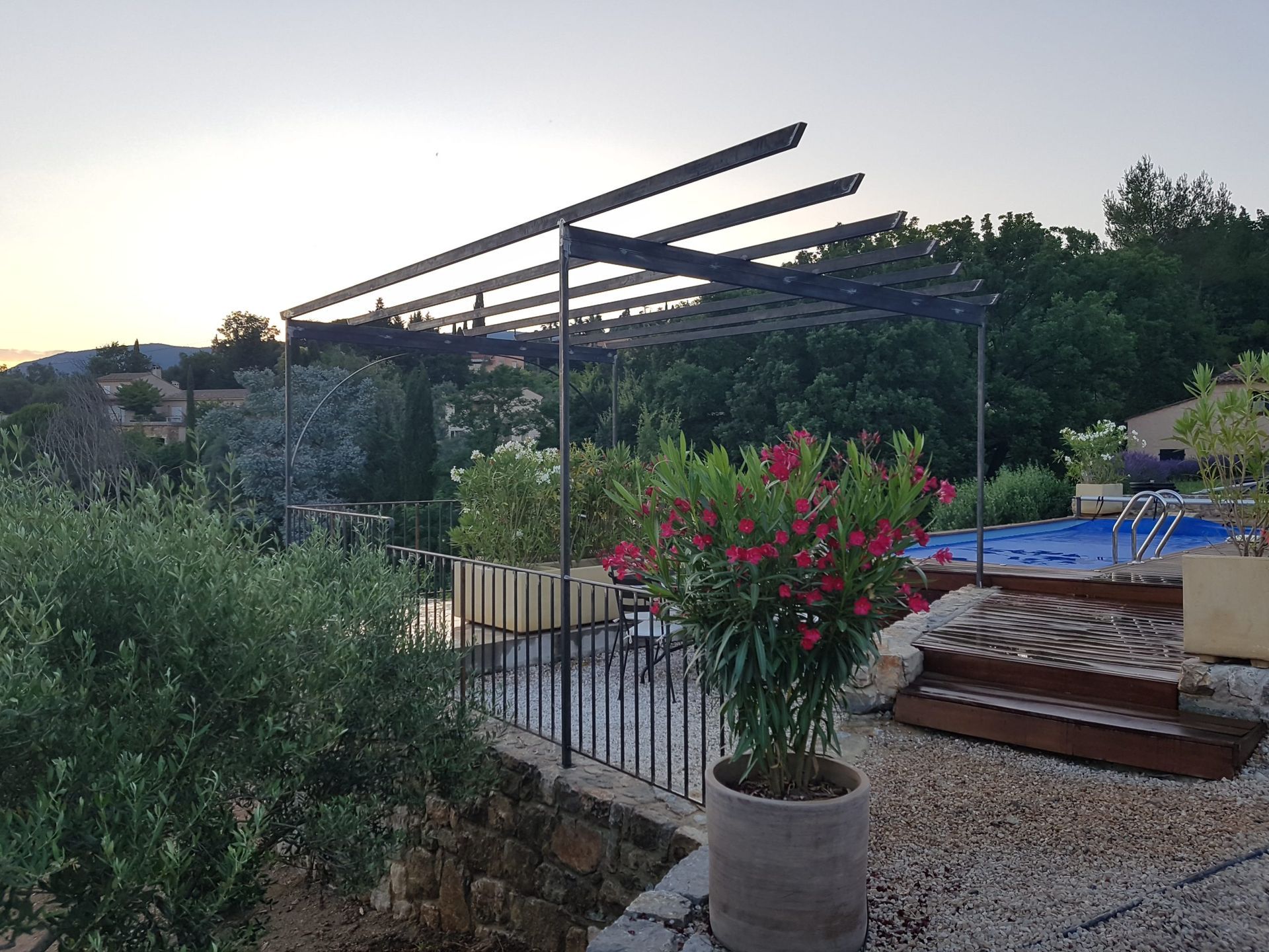 Jardin-terrasse au crépuscule avec pergola, fleurs roses en pot, marches et piscine en arrière-plan