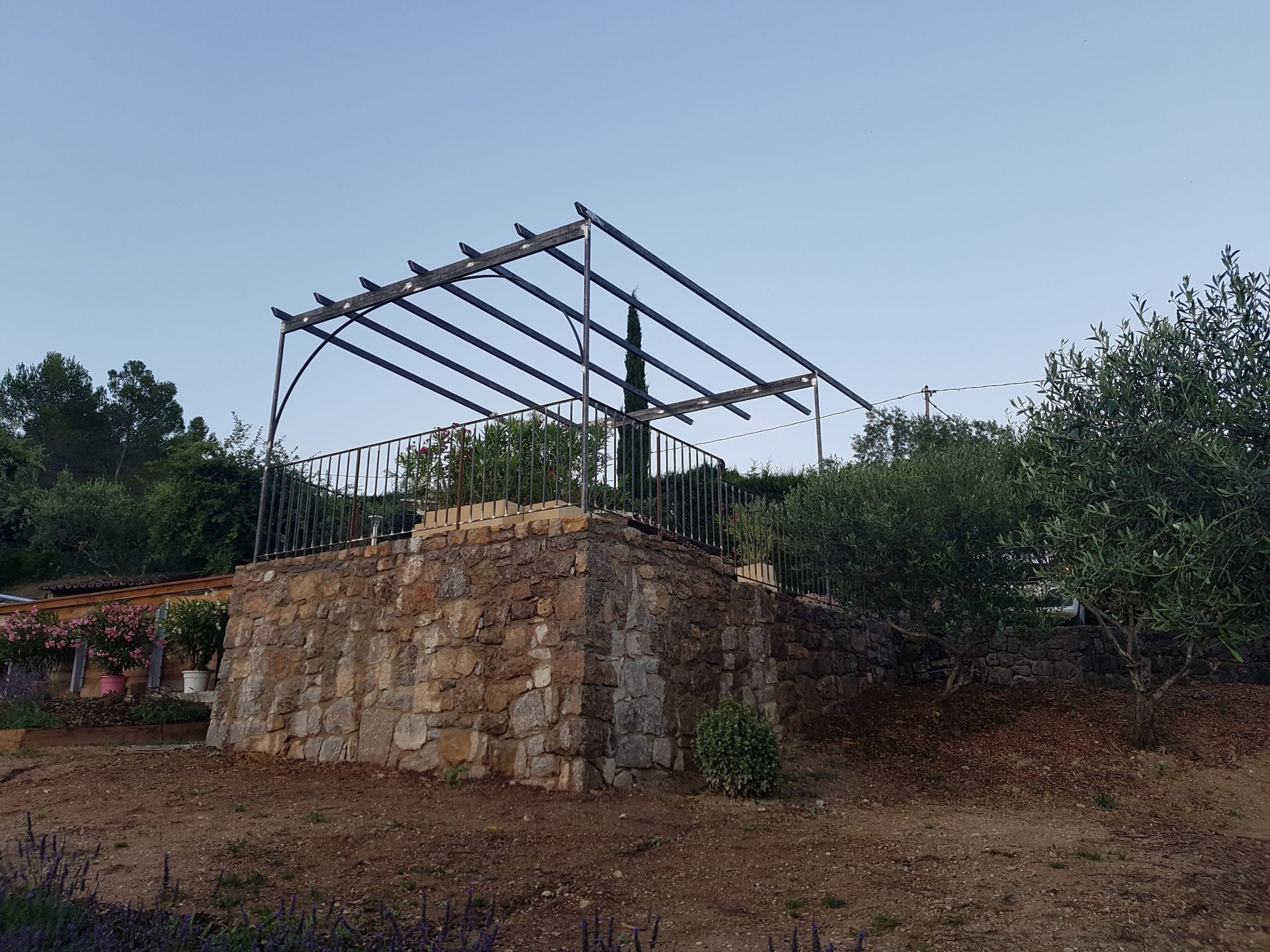 Plateforme en pierre avec une charpente métallique en construction sur un versant boisé