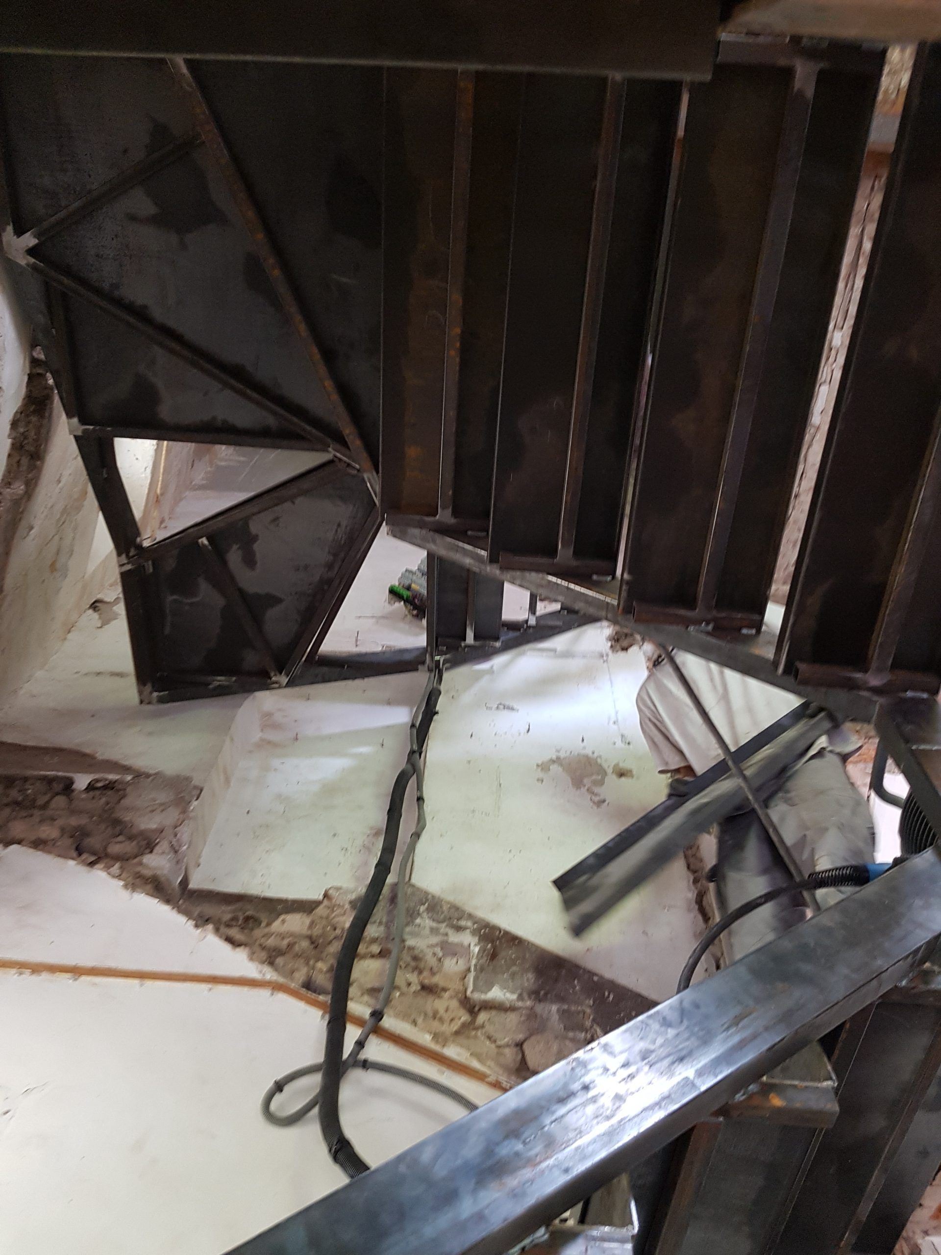 Escalier métallique effondré dans un intérieur endommagé, avec des débris éparpillés sur le sol