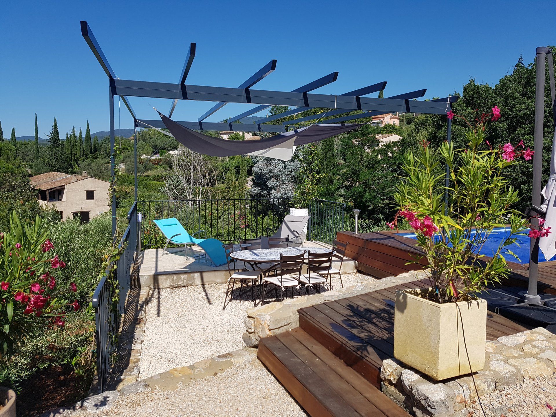 Patio ensoleillé avec chaises longues, pergola ombragée et fleurs colorées sous un ciel bleu