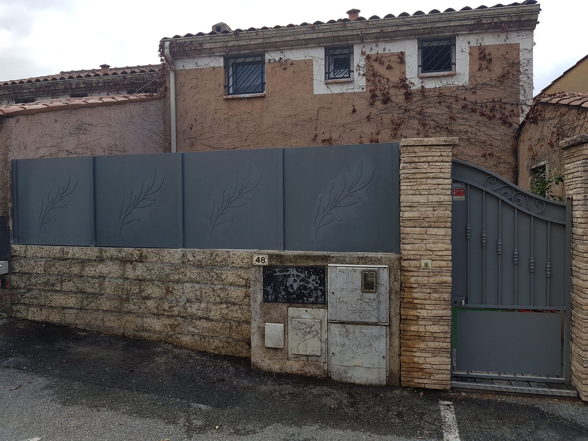 Ancien bâtiment en stuc avec une clôture et un portail en métal gris le long d'un chemin de gravier