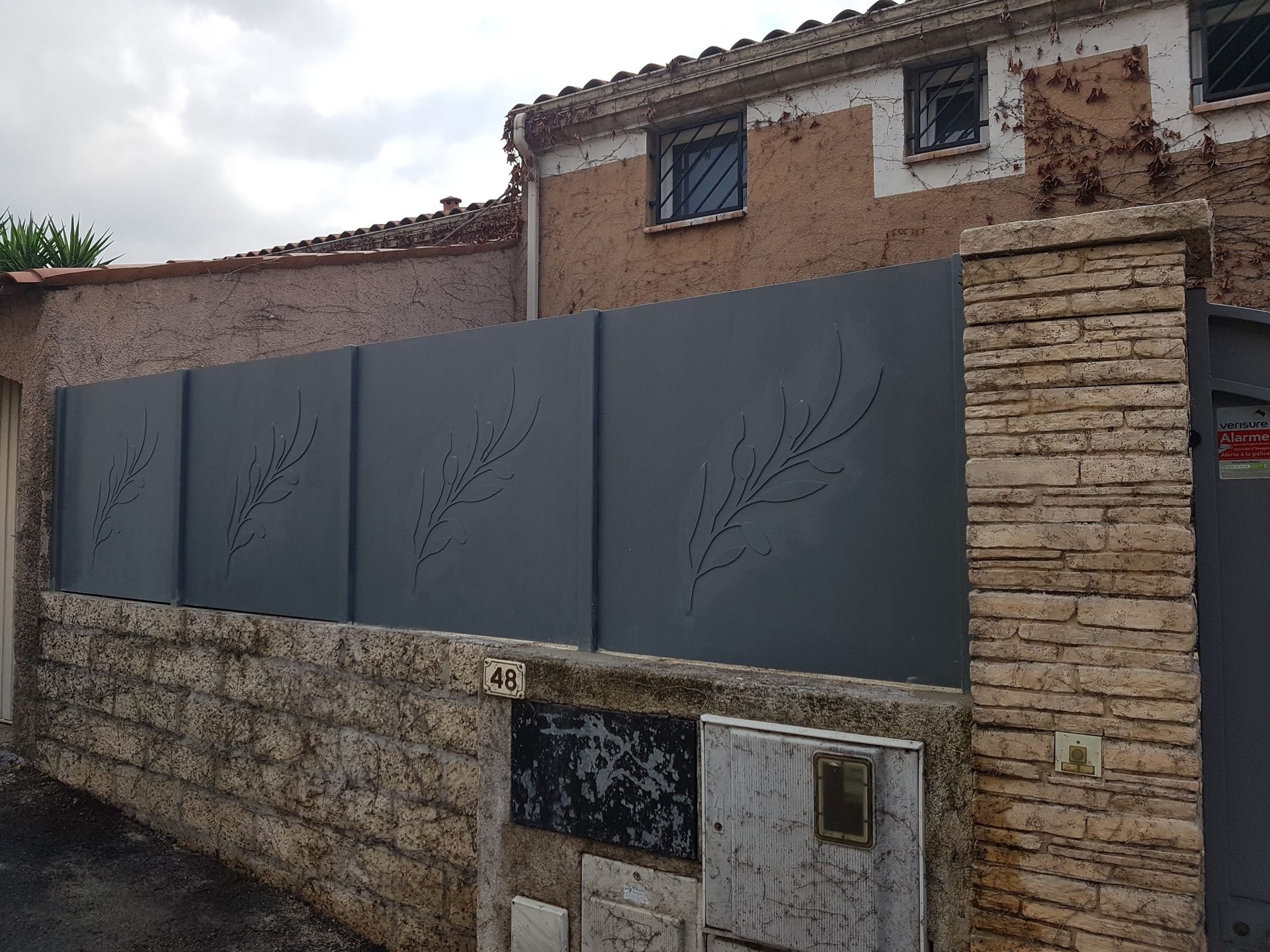 Panneaux d'intimité gris sur un mur de pierre devant une maison rustique et un portail
