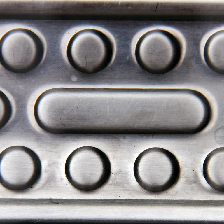 Surface métallique avec des bosses circulaires en relief et une longue forme rectangulaire arrondie ressemblant à un bouton.