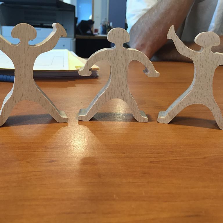 Trois petites figurines en bois aux bras levés, posées sur une table en bois.