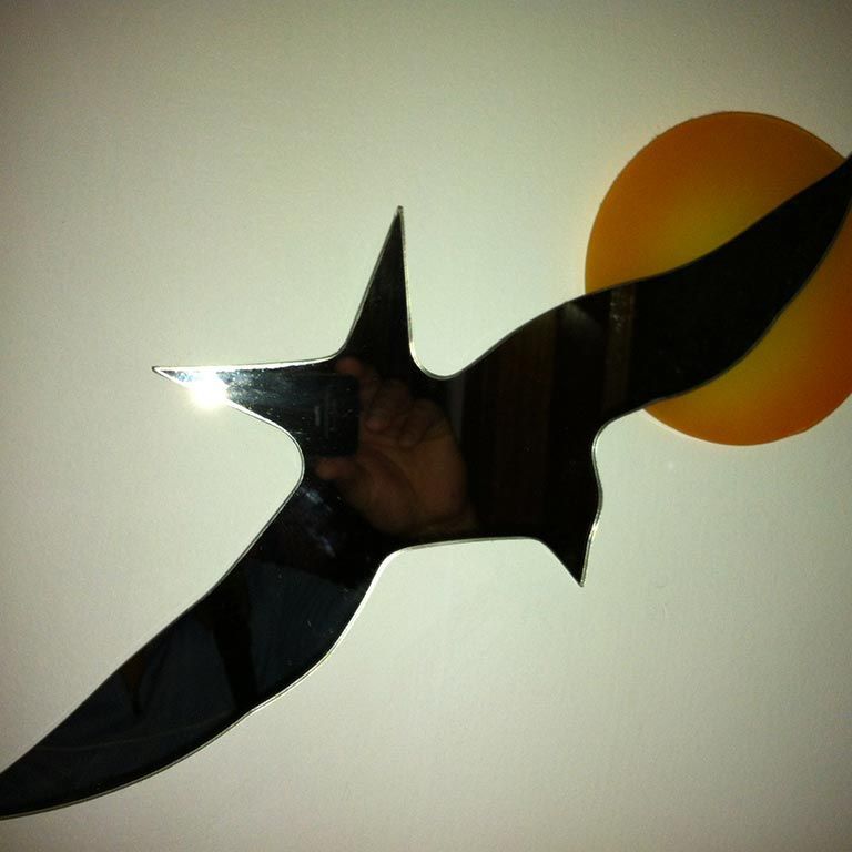 Silhouette d'un oiseau noir aux ailes déployées sur fond clair, près d'un cercle orange