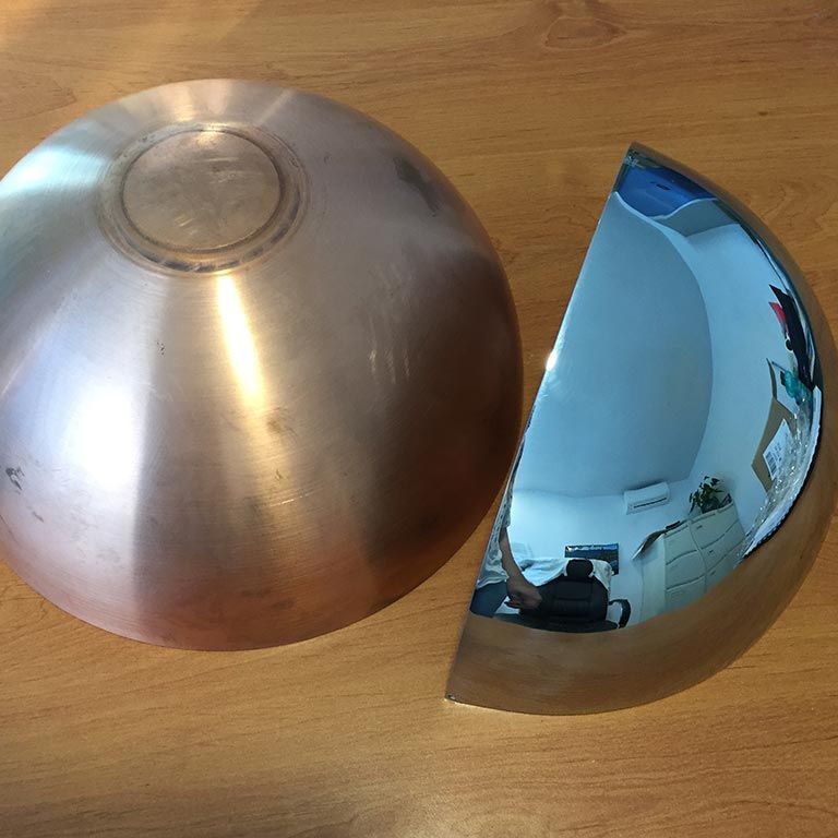 Deux demi-bols en métal brillant posés sur une surface en bois, l'un en argent brossé et l'autre en bleu poli miroir.