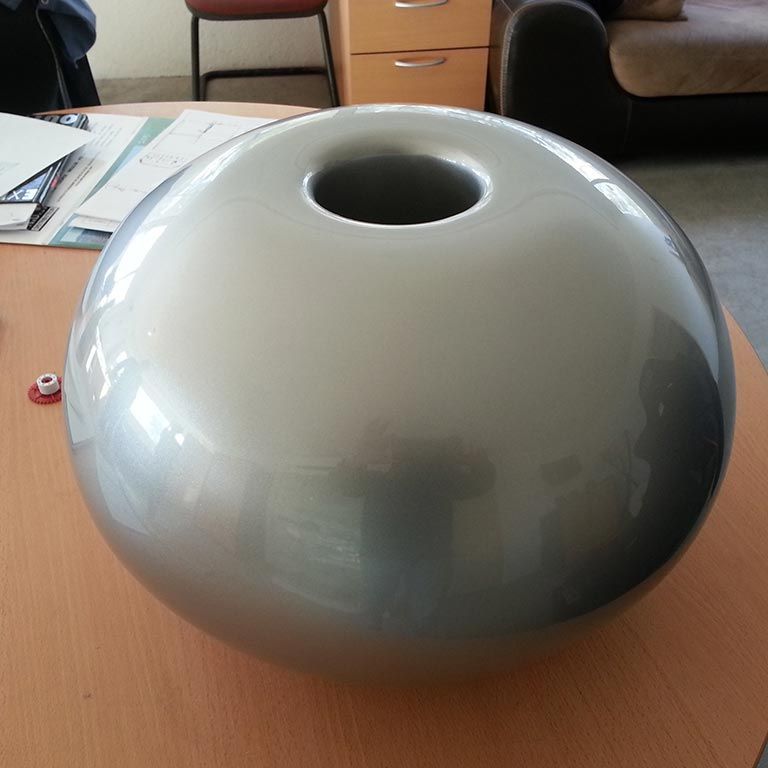 Vase en céramique grise, à corps rond et ouverture circulaire, posé sur une table en bois.