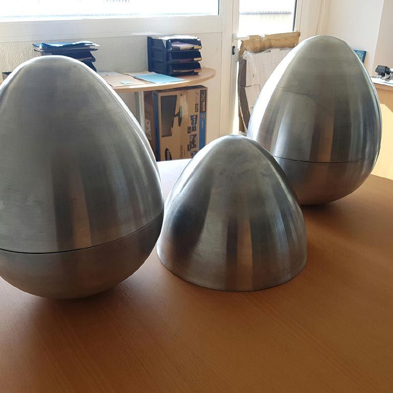 Trois récipients métalliques en forme d'œuf et une pièce en forme de dôme sont disposés sur une table en bois dans une pièce lumineuse.