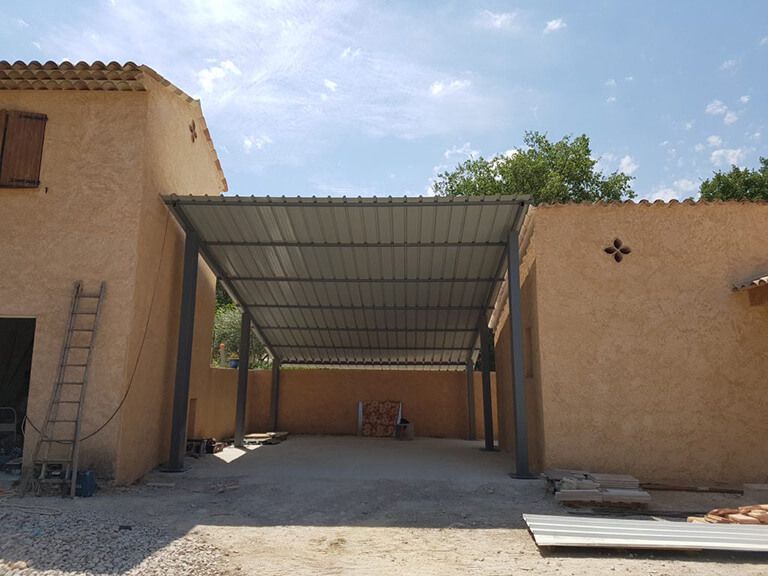 Cour intérieure couverte entre des bâtiments en stuc beige avec un toit en métal et une échelle sur la gauche.
