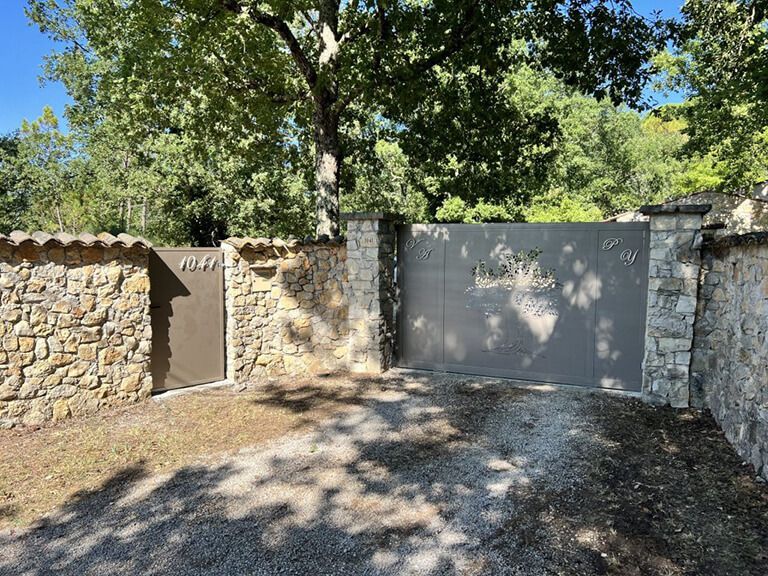 Mur en pierre avec un portail métallique fermé sous des arbres dans une cour ensoleillée