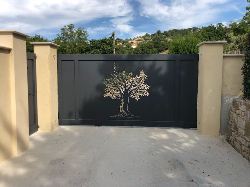 Portail noir orné d'un motif d'arbre entre des murs beiges sous un ciel partiellement nuageux