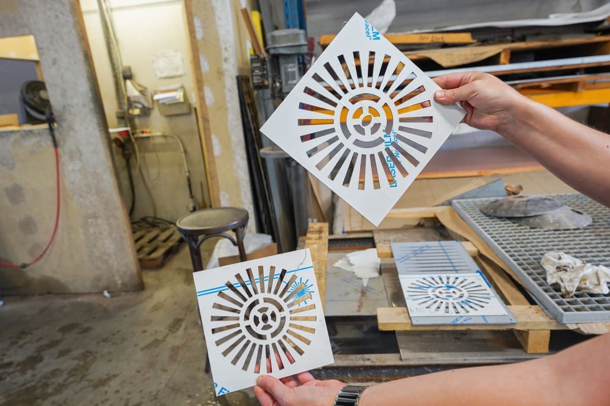 Des mains tiennent deux feuilles de pochoirs décoratives blanches à motifs radiaux orange et noirs dans un atelier.