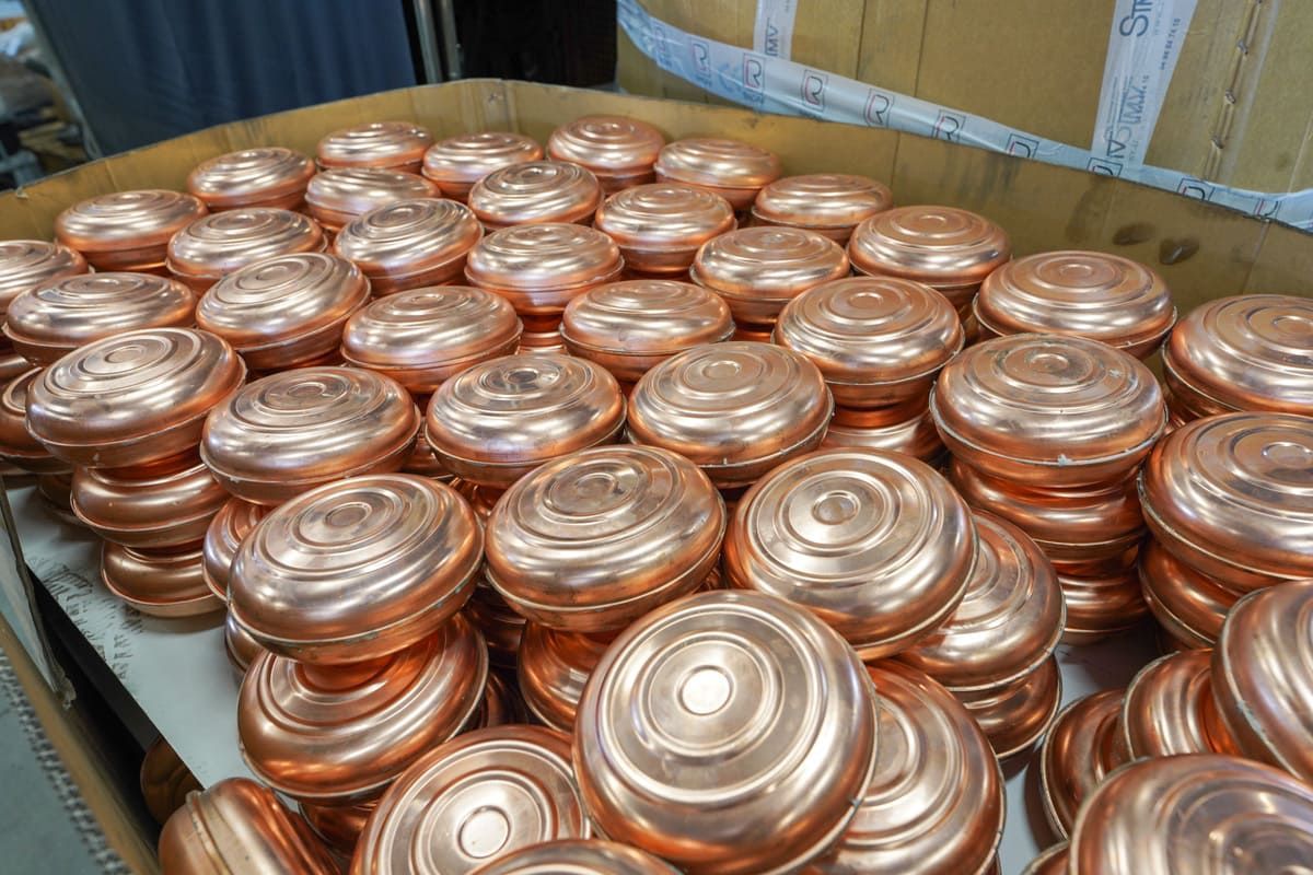 Des piles de couvercles ou de disques métalliques couleur cuivre, entassées dans une boîte en carton sur le sol d'un entrepôt