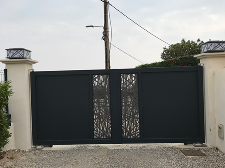 Portail d'allée en métal noir entre des piliers couleur crème et une entrée en gravier