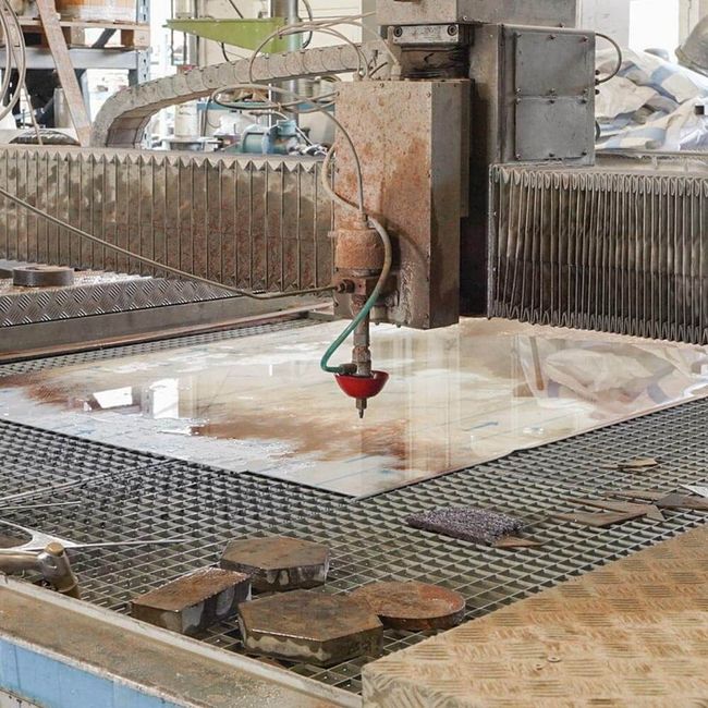 Machine de découpe industrielle au jet d'eau en train de découper une dalle de pierre dans un atelier