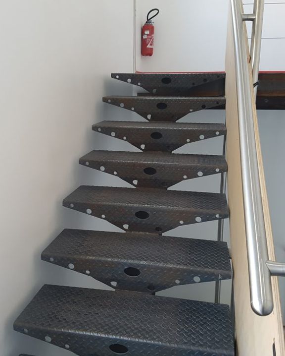 Escalier en colimaçon en métal noir avec une rampe chromée et un extincteur rouge sur le palier.