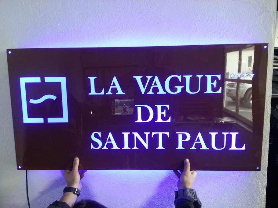 Une enseigne lumineuse bleue portant l'inscription LA VAGUE DE SAINT PAUL est brandie à l'intérieur.